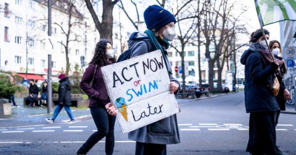 Protestor holding a banner saying Act now or swim later by Mika Baumeister on Unsplash